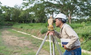 Surveyor using a total station beside a sloped drainage swale for a topographic survey in Oklahoma City