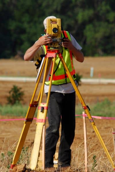 Licensed land surveyor in Oklahoma City using surveying equipment to measure property elevation for an elevation certificate.
