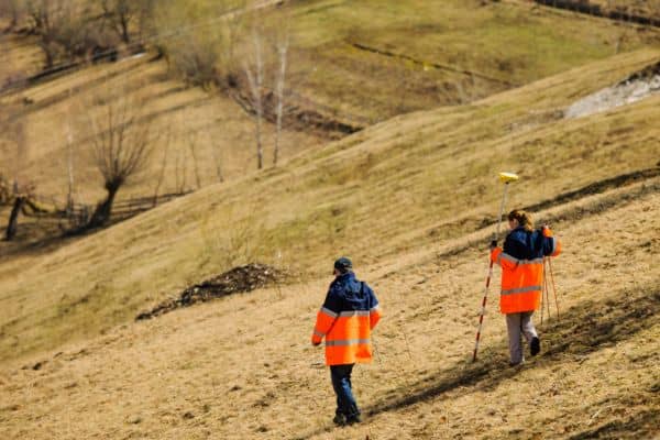 Surveyors walking a sloped site in Oklahoma City with equipment to prepare for a topo survey and record land features
