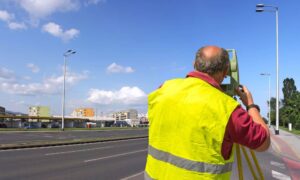 Surveyor using total station beside a city roadway during an ALTA Land Title Survey for infrastructure development