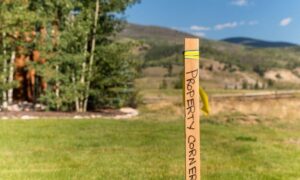 Wooden stake labeled "Property Corner" marking the boundary line during a boundary line survey on a residential property with mountains in the background.