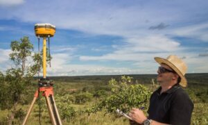 Land surveying professional using a GPS receiver on a tripod to collect accurate site data under a bright sky