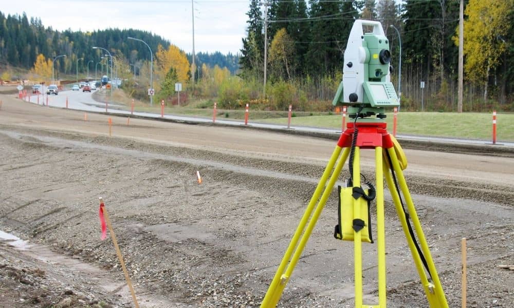 Land surveying equipment set up beside an active road expansion project with visible right-of-way markers