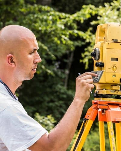 Land surveyor using a total station during a topographic survey to measure elevation and map terrain