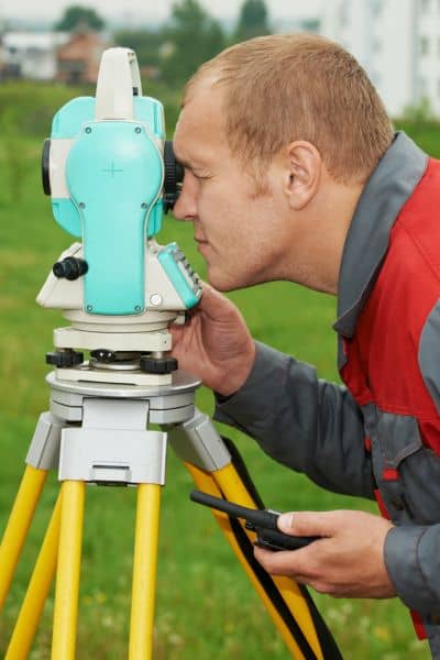 A cadastral surveyor using a total station to measure and confirm a property boundary on-site