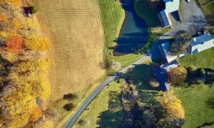 Aerial view of a rural property with several buildings, a driveway, and surrounding farmland, providing a clear view of the property for a property line survey